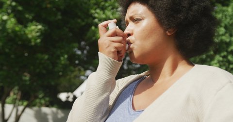 Video of plus size african american woman using inhalator outdoors. health and astma awareness concept.
