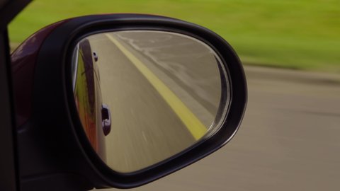 View in the rear view side mirror of a automobile, driving a red car along the road