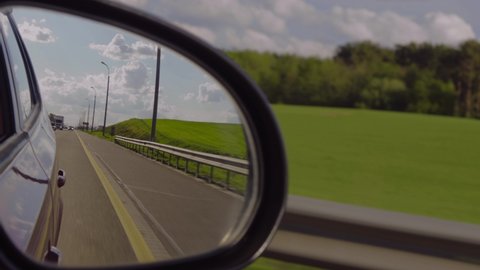View in the rear view side mirror of a automobile, driving a red car along the road