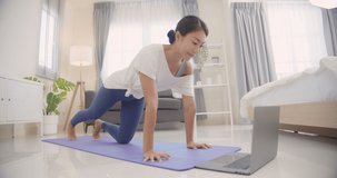 Beautiful happy young Asian woman online yoga classes  in her living room on weekends.Online learning at home .Slow motion.Healthy lifestyle concept.