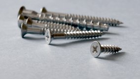 close up video of some screws, with cross head, on grey background and a hand is taking or putting a screw in the background, out of focus. little self-tapping screw in main plan.Industrial background