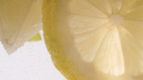 Slow Motion Macro shot of a lemon slice in water bubbles, Soft Drink with Ice, Bubbles, Mint and Lemon. Close Up Refreshment sparkles lemon soda and Cold Summer Drink.