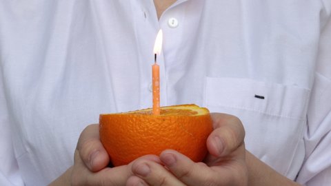 girl holding in both hands a half of orange fruit with a lit candle. celebrate birthday without cake. healthy food concept. no sugar and no sweets. healthy fruit instead of birthday cake. diet, slim