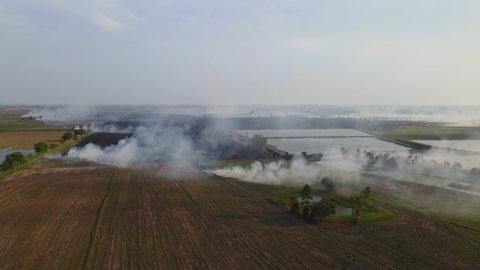 Descending aerial footage revealing a newly tilled field and smoke rising from burning grass, Grassland Burning, Pak Pli, Nakhon Nayok, Thailand.