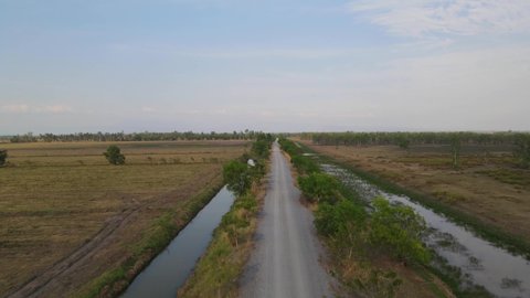 Aerial ascending footage revealing this farm road with canals on both sides and a beautiful horizon, Pak Pli, Nakhon Nayok, Thailand.