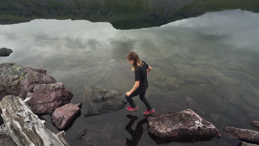 Boy climbs on rocks next to mirrored lake in Swedish Lapland with insects
