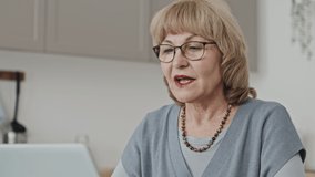 Elderly woman sitting at home and discussing something on online video call on laptop while learning or working remotely