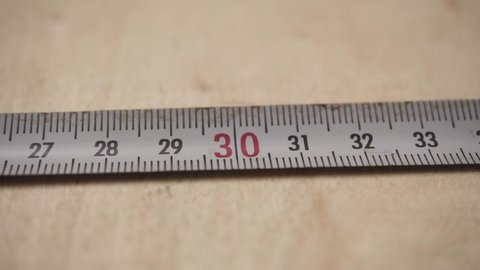 Tape measure tool on wooden background. Flexible ruler. Measure size or distance. Metal strip with linear measurement markings. Focus on 30 centimeter, cm, inch.