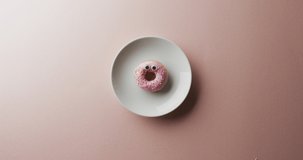Video of donut with icing on white plate over pink background. colourful fun food, candy, snacks and sweets concept.