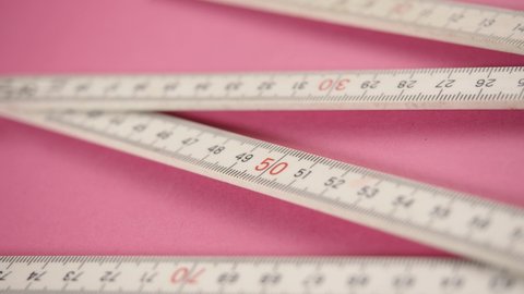Folding Metric Carpenter Ruler on pink background. Tape measure tool. Flexible, collapsible. Measure size or distance or length. Plastic strip with linear measurement markings. Calculation centimeter.