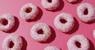 Video of donuts with icing on pink background. colourful fun food, candy, snacks and sweets concept.