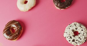 Video of donuts with icing on pink background. colourful fun food, candy, snacks and sweets concept.