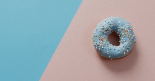 Video of donut with icing on blue and pink background. colourful fun food, candy, snacks and sweets concept.