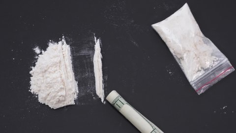 A white substance in a transparent bag, a dollar bill rolled into a tube removes tracks of powder on a black table. The concept of drug addiction, drug use, illegal action. Stop motion animation.