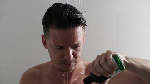 Young man in the shower washing hair with cosmetic shampoo.