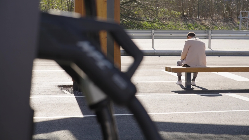 Man Waiting And Sitting On The Bench At Charging Station Under The Sun. - wide | Shutterstock HD Video #1088846011
