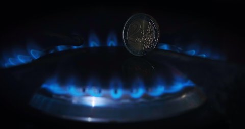 Blue flame of gas stove with 2 euro coin on black background. Kitchen burner turning on. Natural gas inflammation
