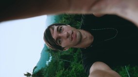 Vertical video portrait of smiling young man tourist making a selfie or video call on green jungle forest background. Young male travels tropical country doing a video chat.