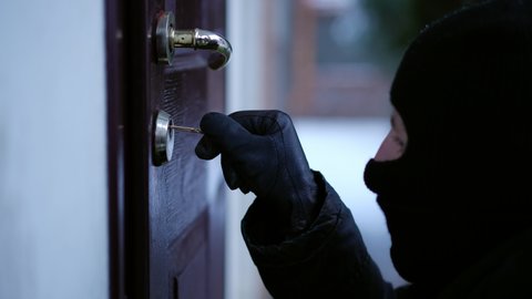 Close-up burglar unlocking entrance door outdoors breaking in house. Side view Caucasian man in mask opening private property robbing. Illegal intrusion and crime concept