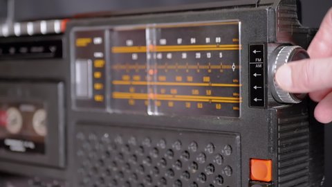 Female Fingers Adjusting the Frequency on an Old Vintage Analog Receiver. Search for a music radio station on a dial scale on panel of a short-wave portable FM radio, player, tape recorder 80s, 90s.