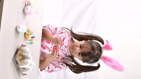Happy little girl with bunny ears painting the egg with fiberpen, preparing for Happy Easter day. Vertical video