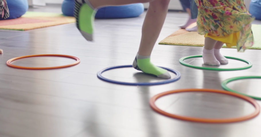Small nursery school children with female teacher on floor indoors in classroom, doing exercise. Jumping over hula hoop circles track on the floor. | Shutterstock HD Video #1088848799