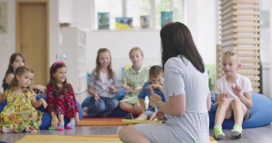 Storytime elementary or primary school teacher reading a story to a group of children in a daycare center.  | Shutterstock HD Video #1088848837