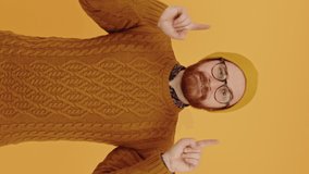 Vertical video European hipster keeps his hands up, points above him portrait isolated copy space yellow background isolated studio shot High quality 4k footage