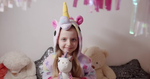 Adorable little 7 year old girl playing in the children's room in a unicorn costume with many toys. Kid joy with unicorn pajamas.