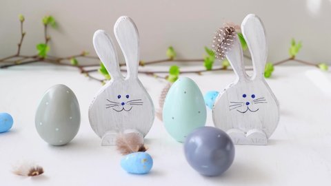 Easter eggs and funny bunnys. Easter eggs are rolling, knocking each other on white table. Happy easter. Festive wooden decoration. Holiday concept, springtime.