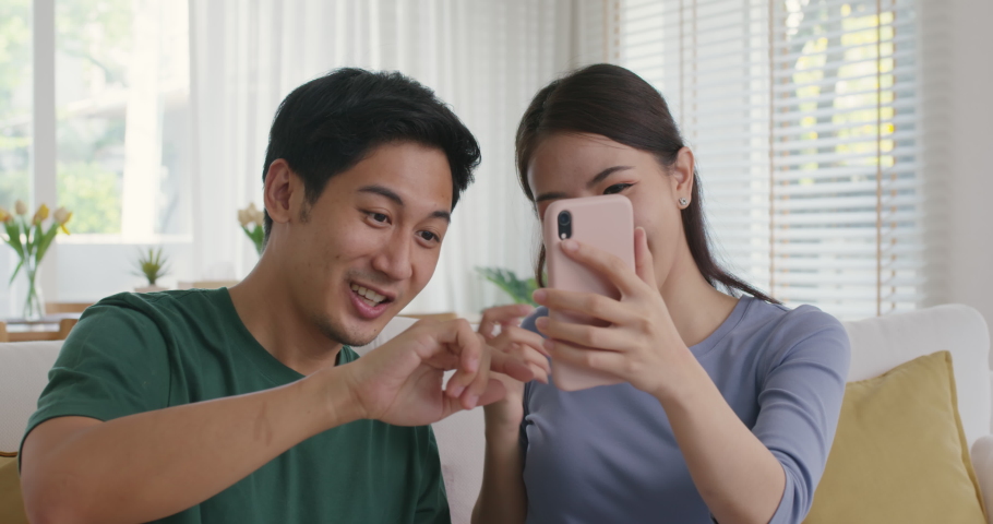 Asia people young couple relax leisure good easy time at cozy sofa home enjoy fun play phone trending filter effect selfie challenge in social media app  reel  viral video story photo shoot