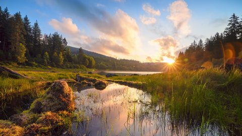Gorgeous morning at the lake, time lapse of beautiful sunrise and colorful moving clouds reflected in the water surrounded by meadows and forests
