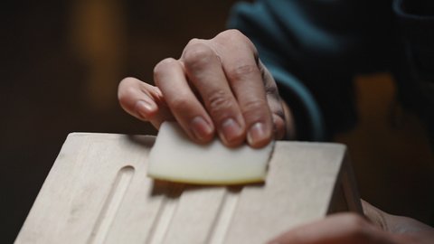 Close-up of an unidentifiable craftsman's hand polishing the corners of a wooden house with sandpaper. Master class on making a birdhouse, slow motion