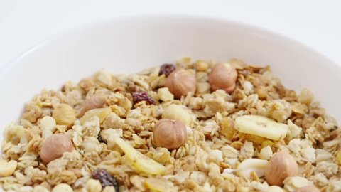 Healthy muesli with fruits, cornflakes and nuts throwing into the white rotating breakfast bowl