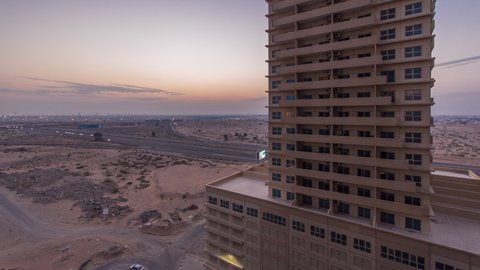 Cityscape with towers in Ajman from rooftop day to night timelapse with towers and traffic on road intersection. Aerial view of illuminated buildings after sunset in the United Arab Emirates.