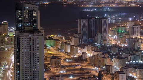 Cityscape of Ajman with traffic on road from rooftop with lights in illuminated buildings at night timelapse. Modern towers and skyscrapers. United Arab Emirates.