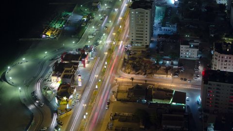 Cityscape of Ajman with traffic on road near shop from rooftop with lights in illuminated buildings at night timelapse. United Arab Emirates.