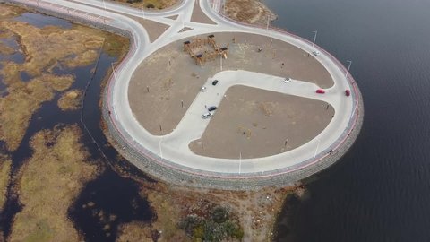 Aerial view from drone of cars driving roundabout traffic circle, parking and children playground near Laguna Nimez ecological reserve on Lago Argentino lake, El Calafate, Patagonia, Argentina