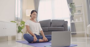 Beautiful happy young Asian woman warming up for an online yoga class in her living room on weekends.Online learning at home .Slow motion.Healthy lifestyle.