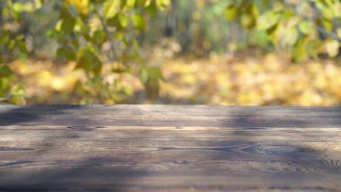 Rustic old wooden table outdoors with autumn leaves falling in the background. Empty table top planks product display with blurred background scene of autumn forest