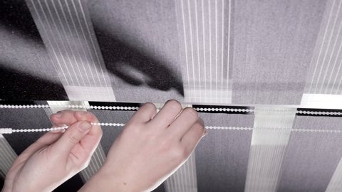 Woman hands pulling string as blinds drop window roller duo system day and night. Close up on roll curtains indoor.