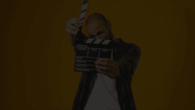 Casual young african american man claps clapperboard against yellow background