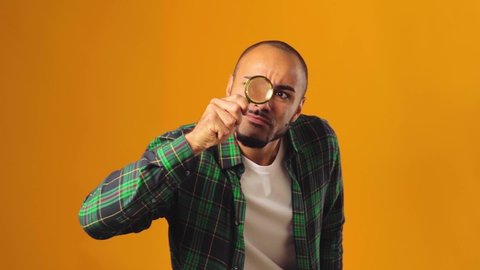 Young african american man looking through magnifying glass against yellow background