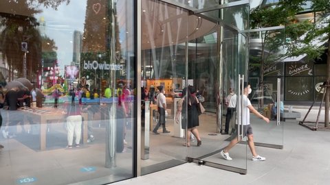BANGKOK, THAILAND - Circa November, 2021: Apple Store at Central World, huge glass window view shopper inside. People walk in the entrance door. Christmas tree in glass window reflection