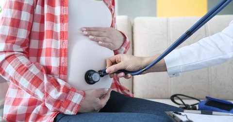 Gynecologist listens with stethoscope to belly of pregnant woman