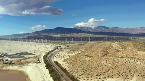 Drone flies over train tracks towards windmill farm in Palm Springs, San Bernardino Mountains in distance.