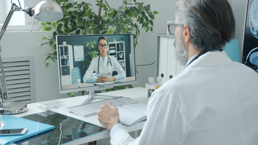 Male doctor talking to female colleague during online video call using computer in hospital. Medical profession and modern technology concept. Royalty-Free Stock Footage #1088873387