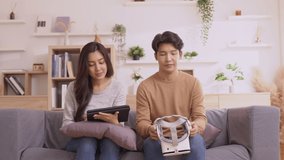 Asian couple playing game and having fun together with virtual reality headset on the sofa.