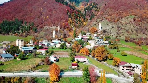 A bird's-eye view of a village or city on a hilly terrain. Mestia settlement in Svaneti in Georgia. The drone flies over the ancient Svan towers against the background of a yellow autumn forest.