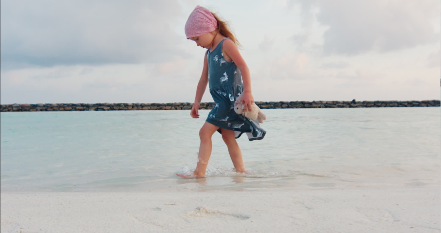 Kid on the beach. Girl walks on the sandy beach during sunset